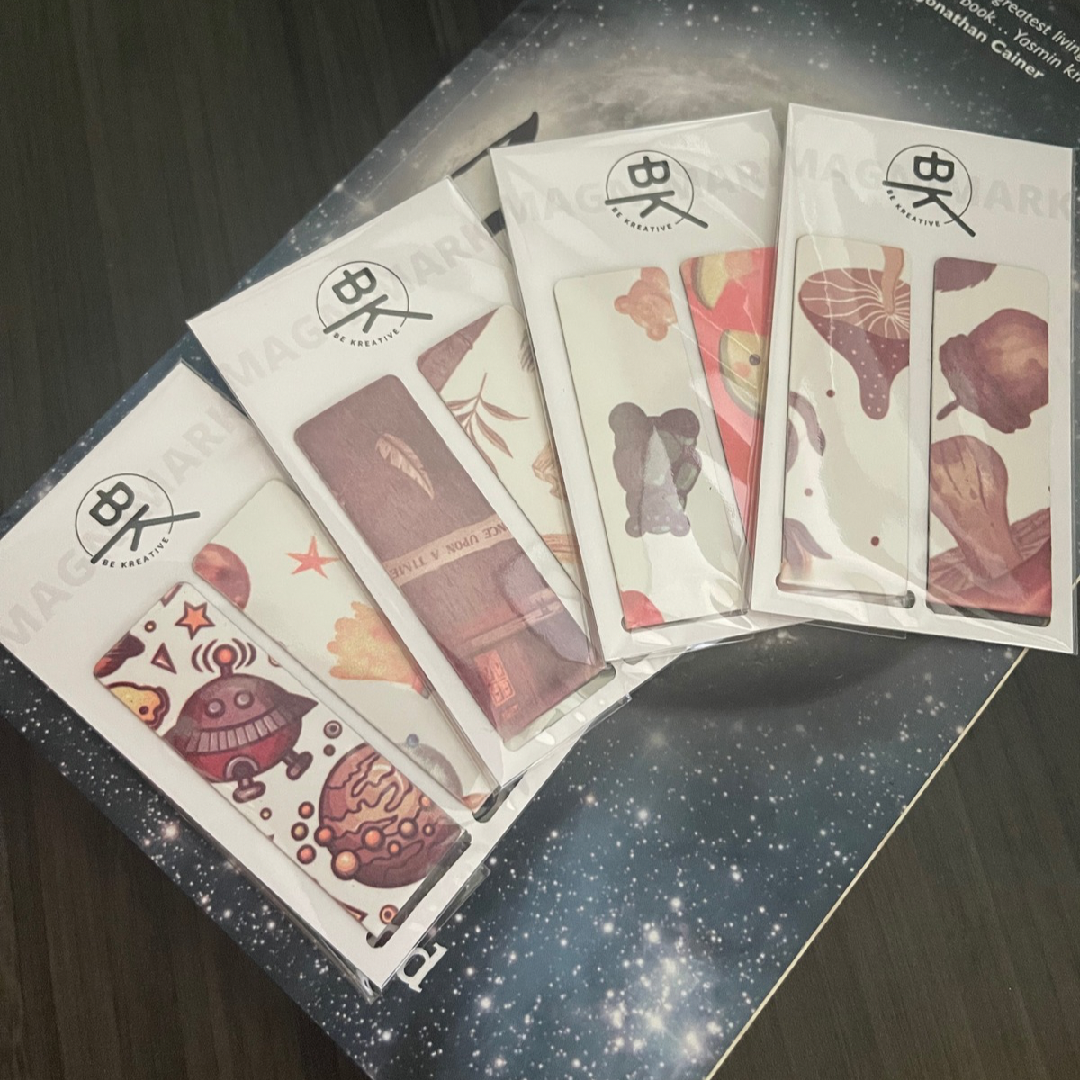 A variety of five creatively designed magnetic bookmarks that are packaged and displayed against a dark, starry background highlighting their unique artistic styles.
Bookmark, magnet bookmark, art designs, cosmic background, creative styles, tattoo collection, package display, unique illustrations, colorful graphics, surface presentation, whimsical themes, galaxy backdrop, visual art, playful designs, personal expression, vibrant colors, fantasy themes, graphic design